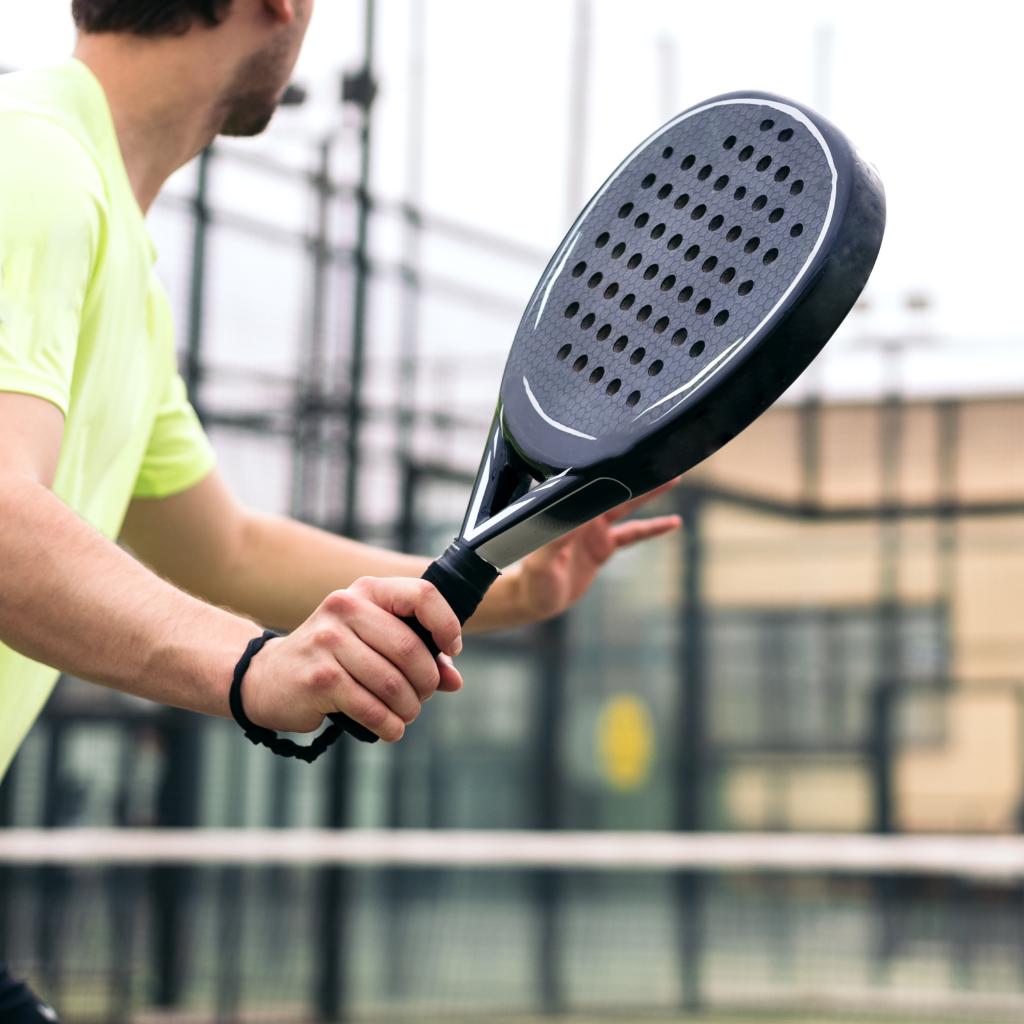 vue partielle d'un joueur de Padel de dos en pleine action de jeu armant son bras qui tient sa raquette près à renvoyer une balle
