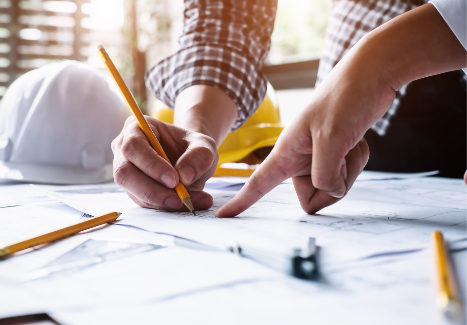 Gros plan sur deux mains écrivant sur ce que l'on devine être des plans d'architecte