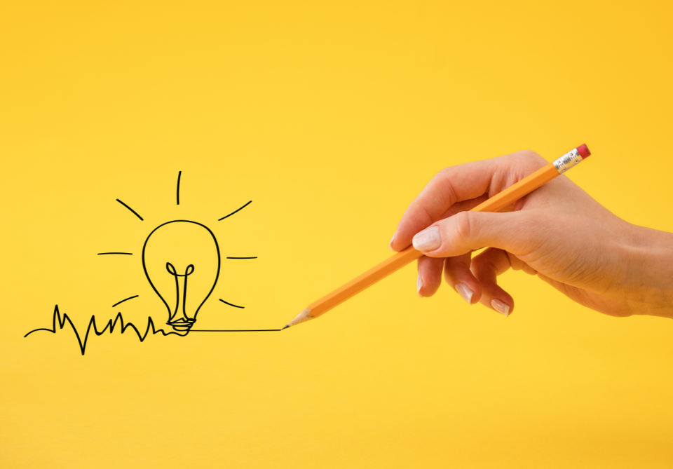 une main tenant un crayon à papier ayant dessinée sur un fond jaune une ampoule illuminée