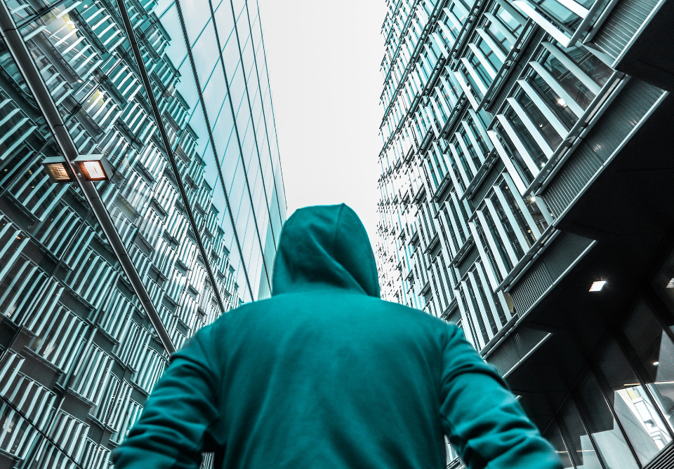 l'illustration de qui sommes-nous est une vue de derrière d'une personne portant un sweat à capuche située entre deux immeubles dont la structure est bleue jade comme la tenue de la personne que l'on ne peut reconnaitre