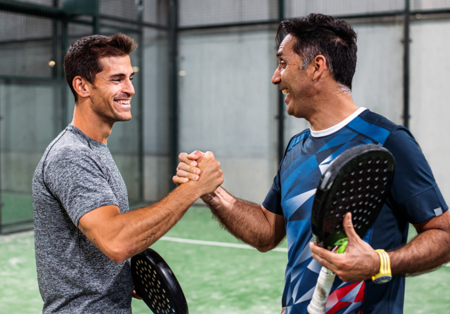 Deux joueurs de padel se serrent la main en souriant au milieu du cours de padel